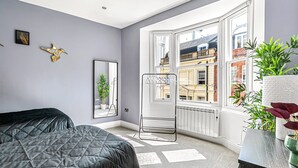 A bedroom with a bed, a radiator, a window with a view of buildings, and a plant on a dresser. - The Lanes Getaway Moments Away From Pier Beach (Brighton)