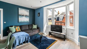 A modern living room with a blue wall, a large window, a sofa, a coffee table, and a TV. - The Lanes in Brighton by Creatick (Brighton)