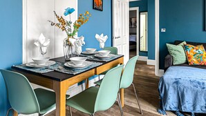 A dining area with a wooden table set for four, green chairs, and a vase with flowers on the wall. - The Lanes in Brighton by Creatick (Brighton)