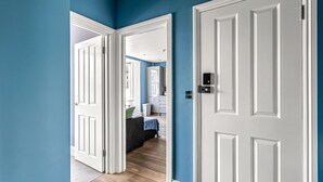 A hallway with a white door leading to a bedroom with a bed and a dresser. - The Lanes in Brighton by Creatick (Brighton)