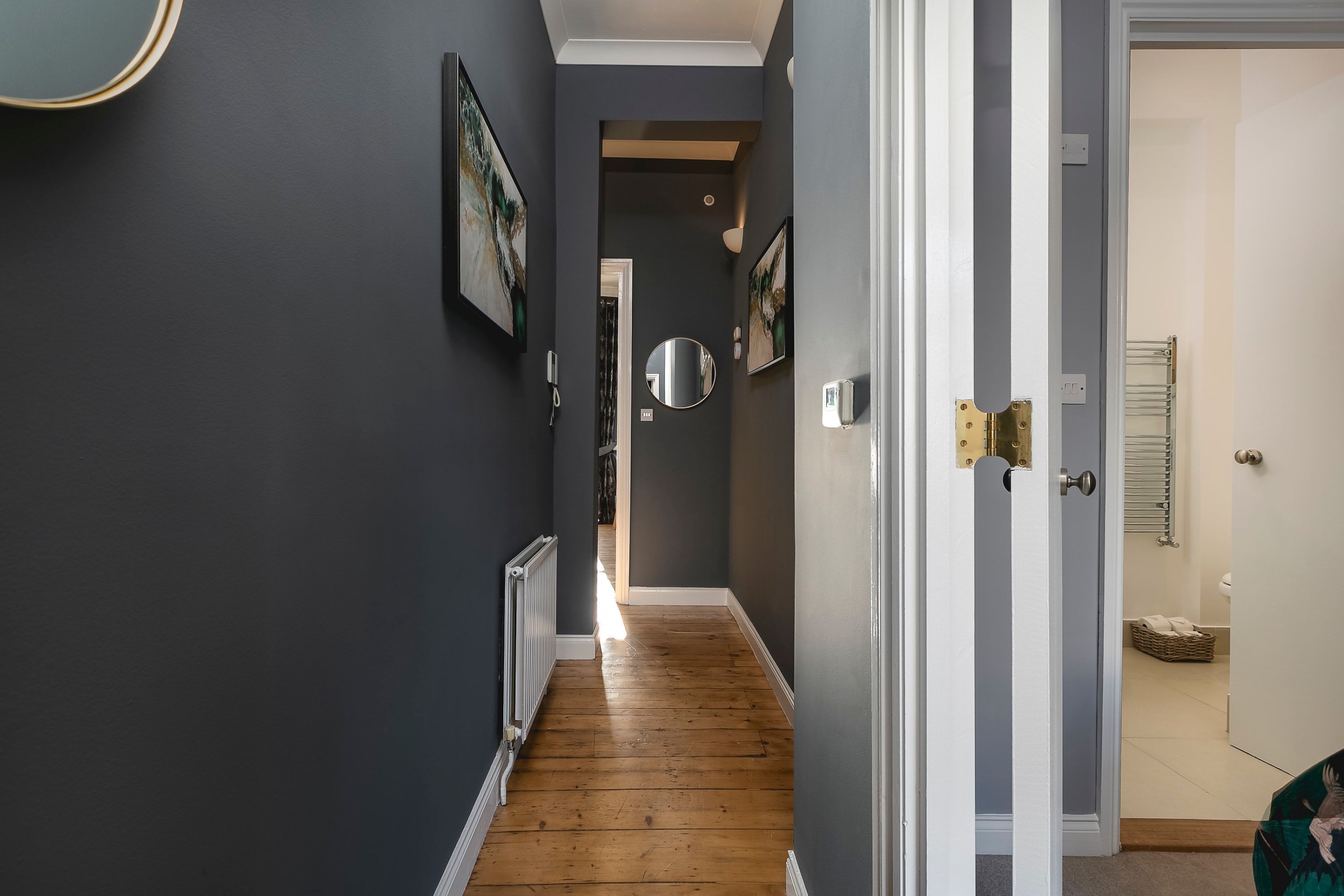A hallway with dark walls, a wooden floor, and a door leading to a bathroom.