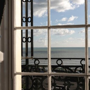 A window with a view of the sea and a metal balcony railing.
