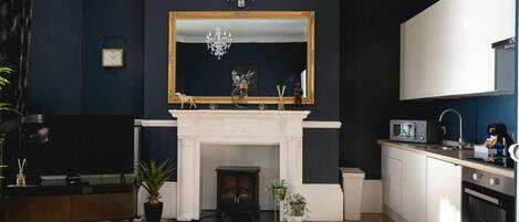 A modern living room with a fireplace, a large mirror, and a kitchen area.