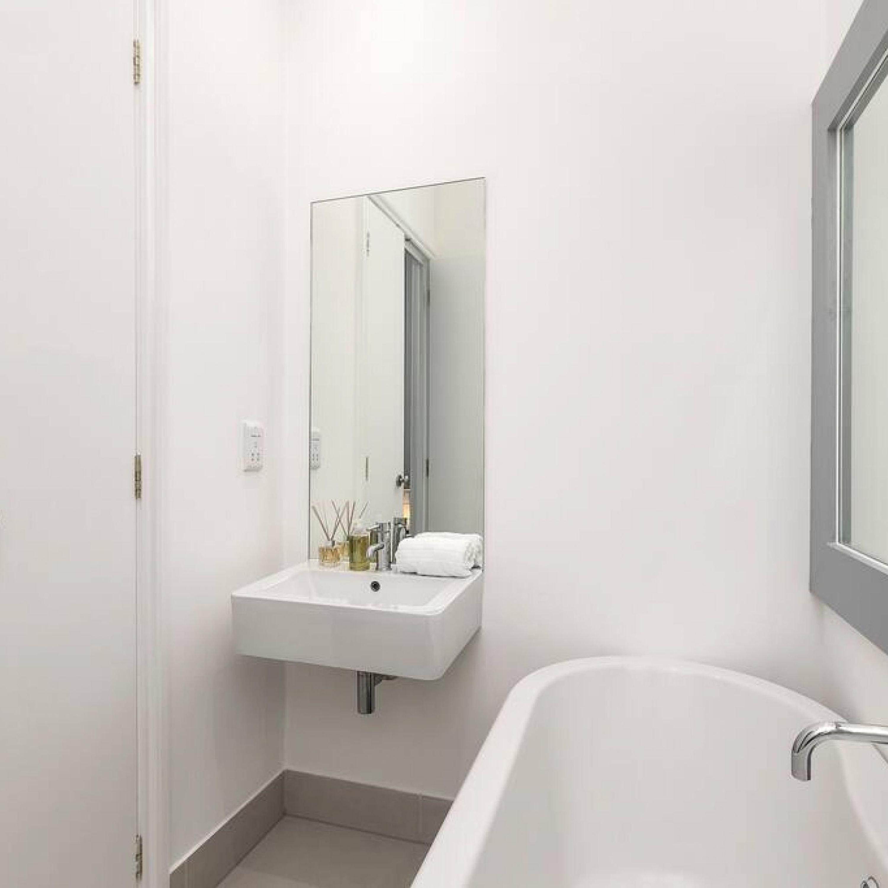A modern bathroom with a white sink, mirror, and bathtub.