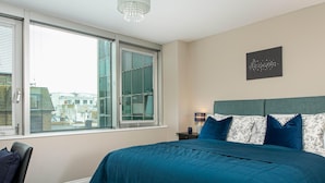 A bedroom with a large bed, a view of buildings through the window, and a chandelier. - Gorgeous 5 Star Location 2 min to Brighton Beach (Brighton)