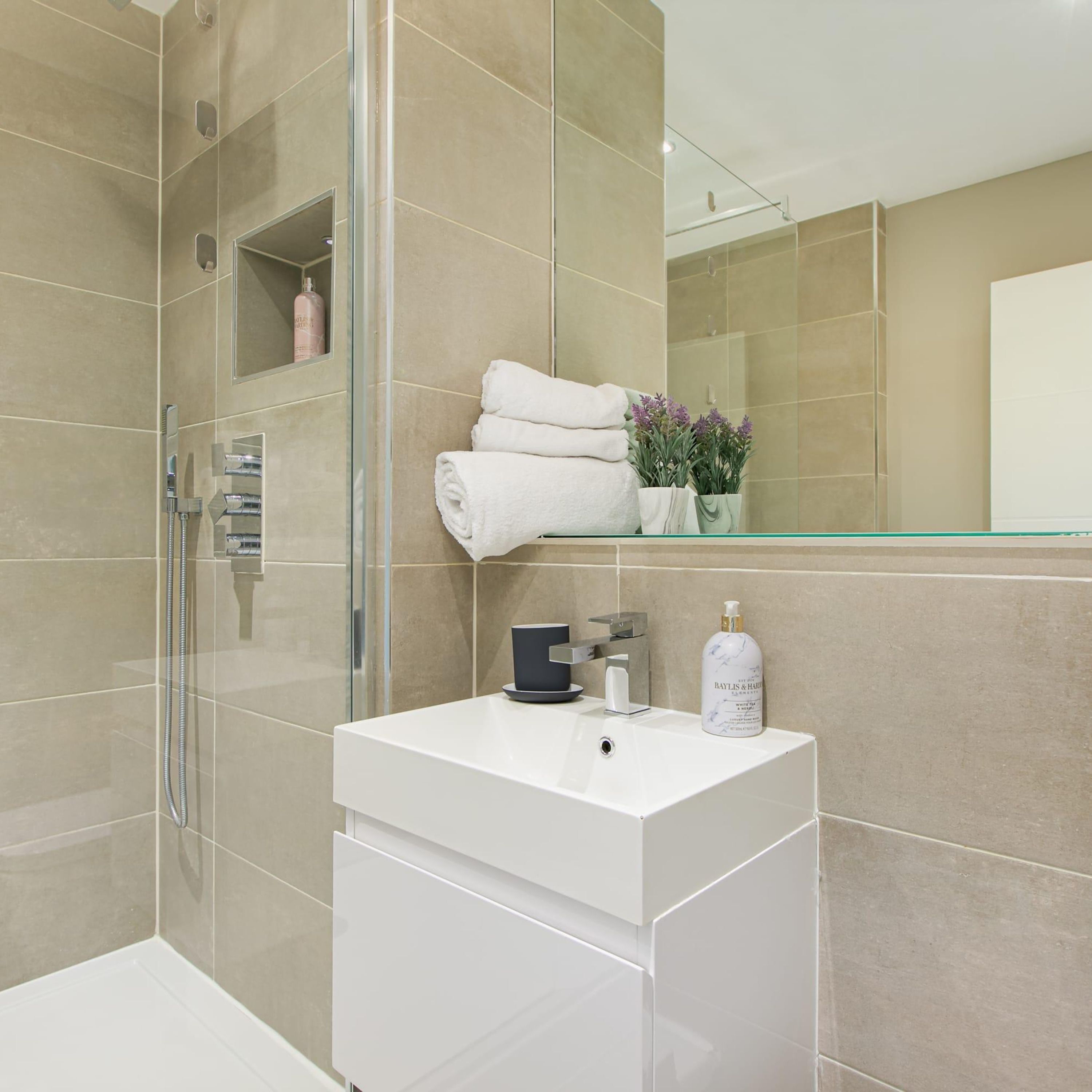A modern bathroom with a glass-enclosed shower, a white vanity with a mirror, and a shelf with toiletries.