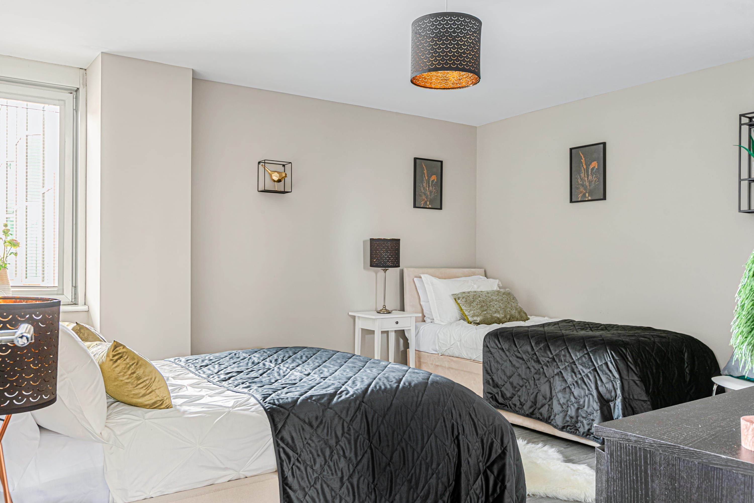 A bedroom with two beds, a nightstand, a lamp, and framed artwork on the wall.