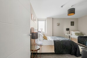 A modern bedroom with a large bed, a smaller bed, a side table, a lamp, and a hanging light fixture.