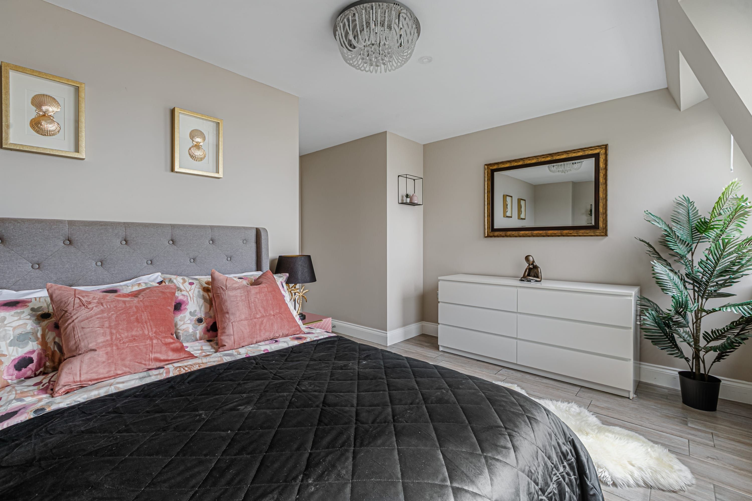A bedroom with a bed, dresser, mirror, and potted plant.