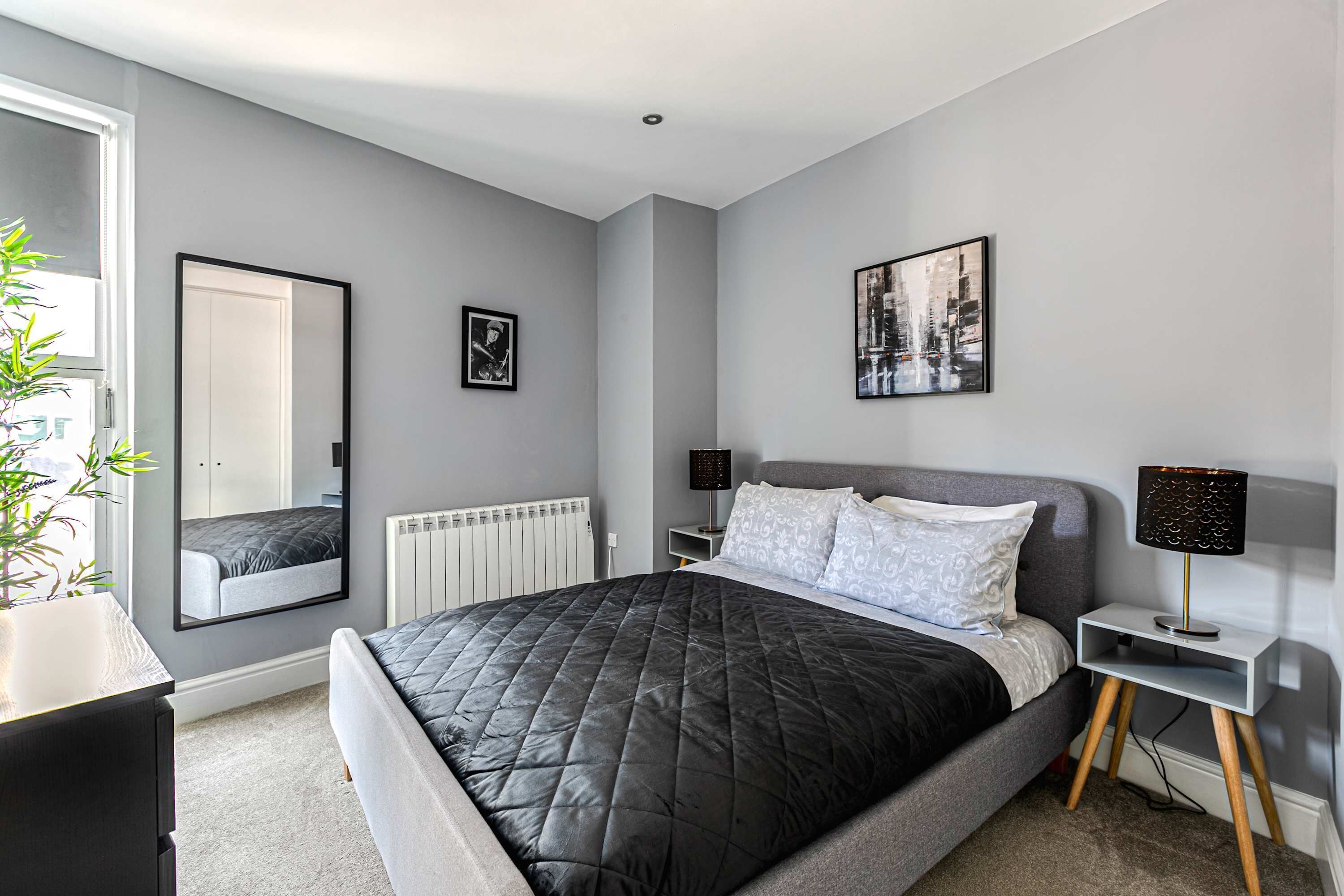 Een moderne slaapkamer met een groot bed, een nachtkastje, een lamp, een spiegel en een radiator.