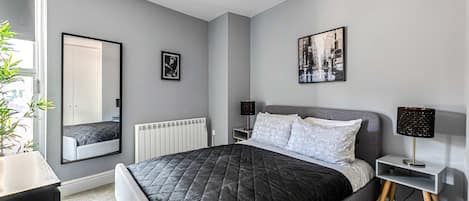 Een moderne slaapkamer met een groot bed, een nachtkastje, een lamp, een spiegel en een radiator.