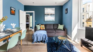 A modern living room with a blue wall, a brown sofa, a glass coffee table, and a TV. - Brighton Lanes Lodge (Brighton)