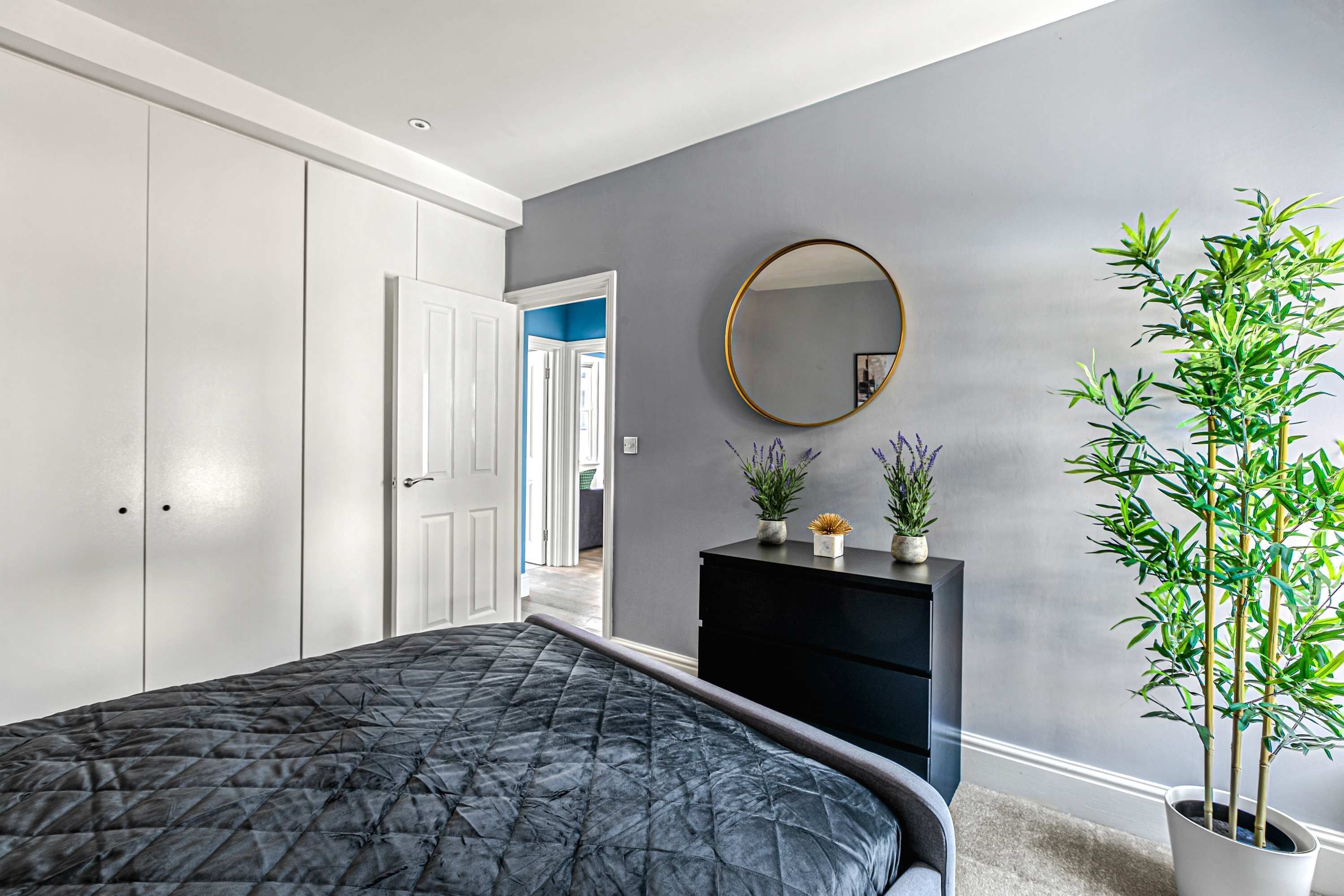 A bedroom with a bed, a dresser, a mirror, and a potted plant.