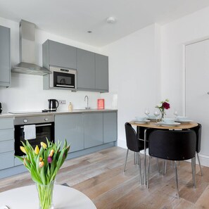 A modern kitchen with grey cabinets, a built-in oven, and a dining area with a round table and black chairs.