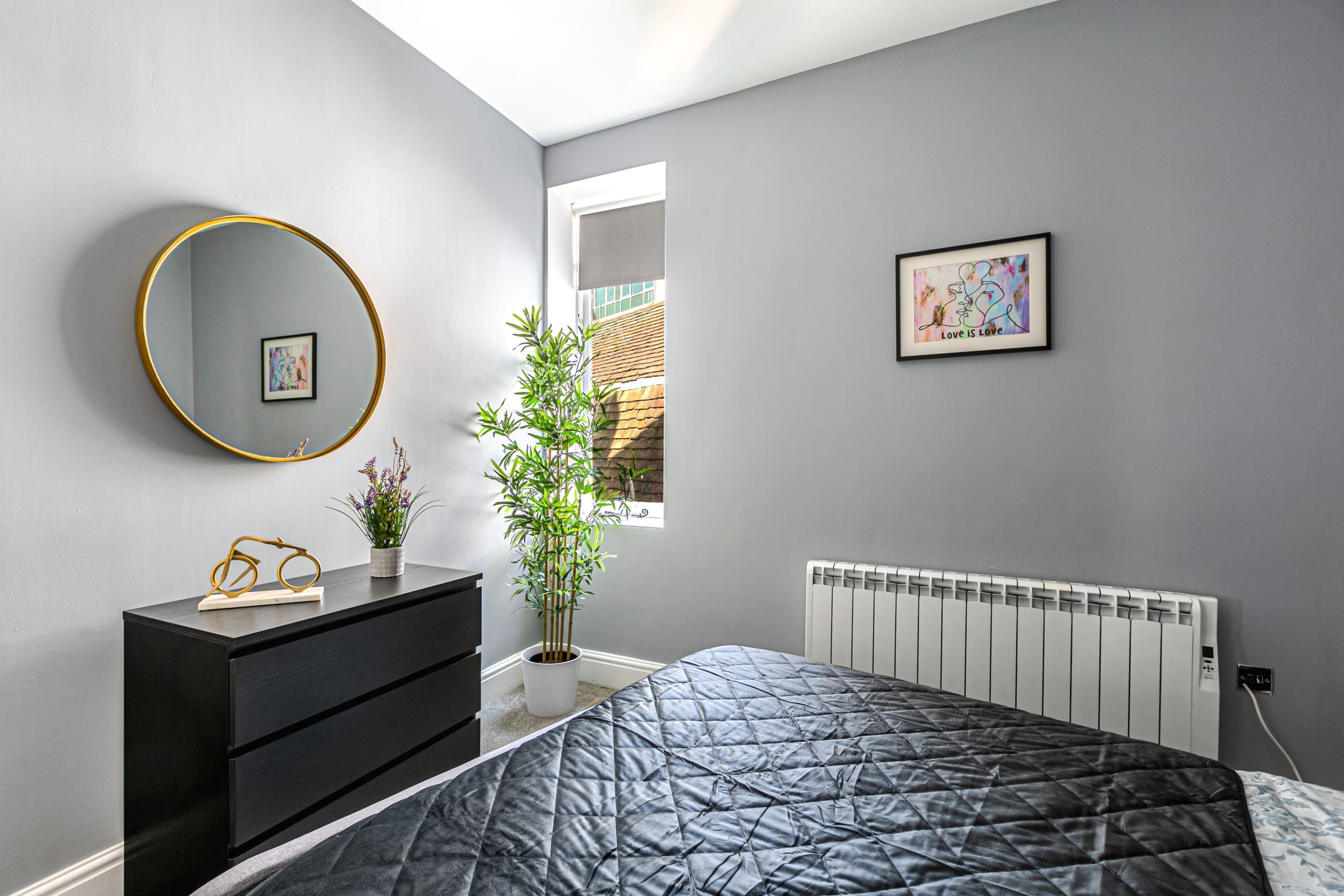 A bedroom with a bed, a dresser, a mirror, a radiator, and a window.