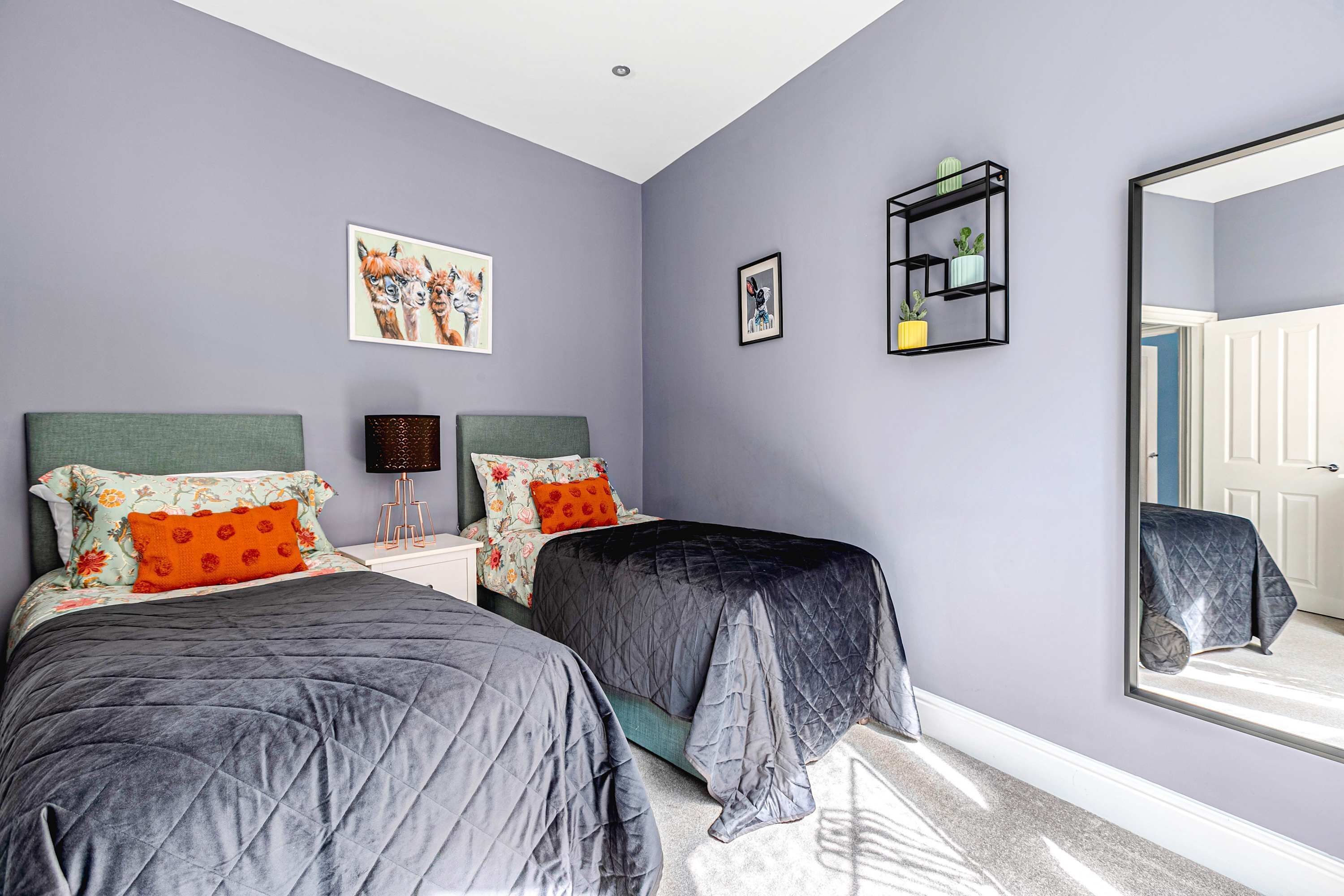 A bedroom with two beds, a large mirror, and artwork on the walls.