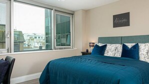 A bedroom with a large bed, a chair, a nightstand, a lamp, and a window with blinds. - Spacious Perfect Location Moments Away From Pier (Brighton)
