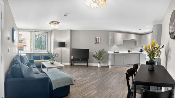 Una sala de estar moderna con un sofá, una mesa de comedor y una cocina con armarios y un lavamanos.