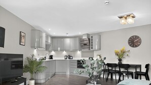 Una cocina moderna con electrodomésticos integrados, una zona de comedor con sillas, una mesa de centro y un reloj en la pared.