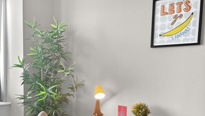 Habitación de esquina con una mesa de madera, una silla, una planta en maceta, una lámpara de pared y un cuadro enmarcado.