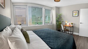 Un dormitorio con una cama, un escritorio, una silla, una planta en maceta y una puerta.