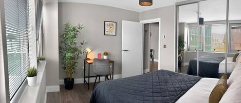 A bedroom with two beds, a desk with a lamp, a potted plant, and a mirror.