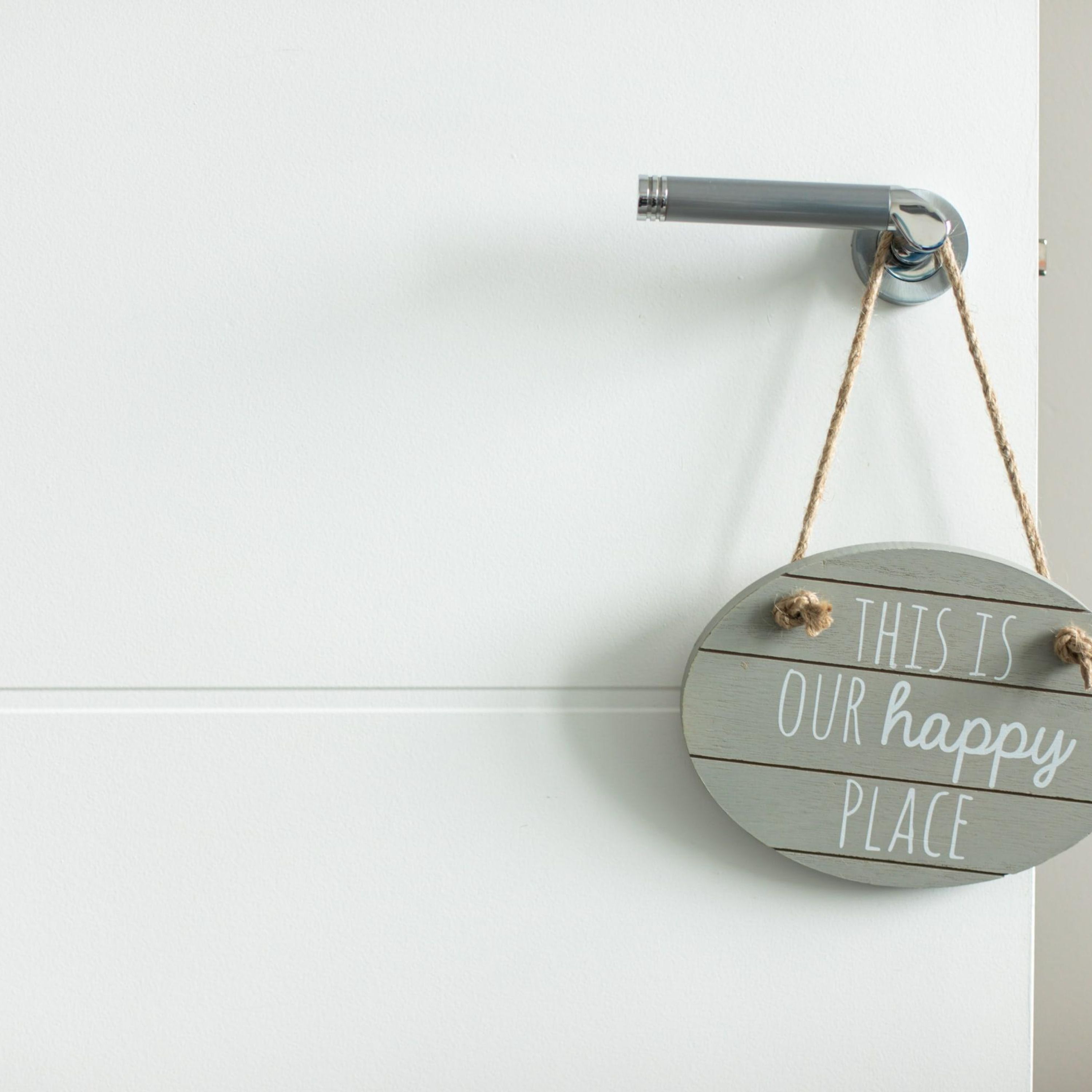 A round sign with the text "THIS IS OUR HAPPY PLACE" hanging on a white wall.