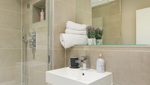 Une salle de bain moderne avec une douche à parois de verre, un meuble-lavabo blanc avec un miroir et une étagère contenant des articles de toilette.