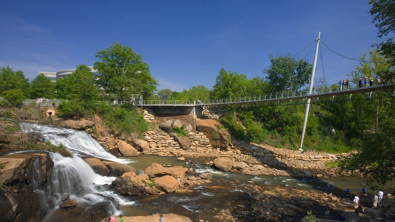 A bridge over a river with a waterfall, surrounded by greenery and a stone structure.