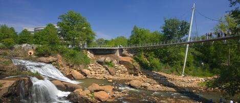 A bridge over a river with a waterfall, surrounded by greenery and a stone structure.