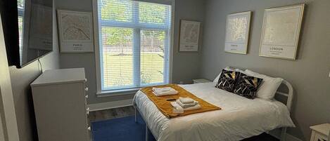 A bedroom with a bed, a ceiling fan, a window with blinds, and framed maps on the wall.