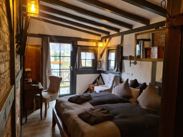 A cozy room with a bed, a chair, a desk, and a window with curtains. - Hotel b&b altes hinterhäusel (Freiberg)