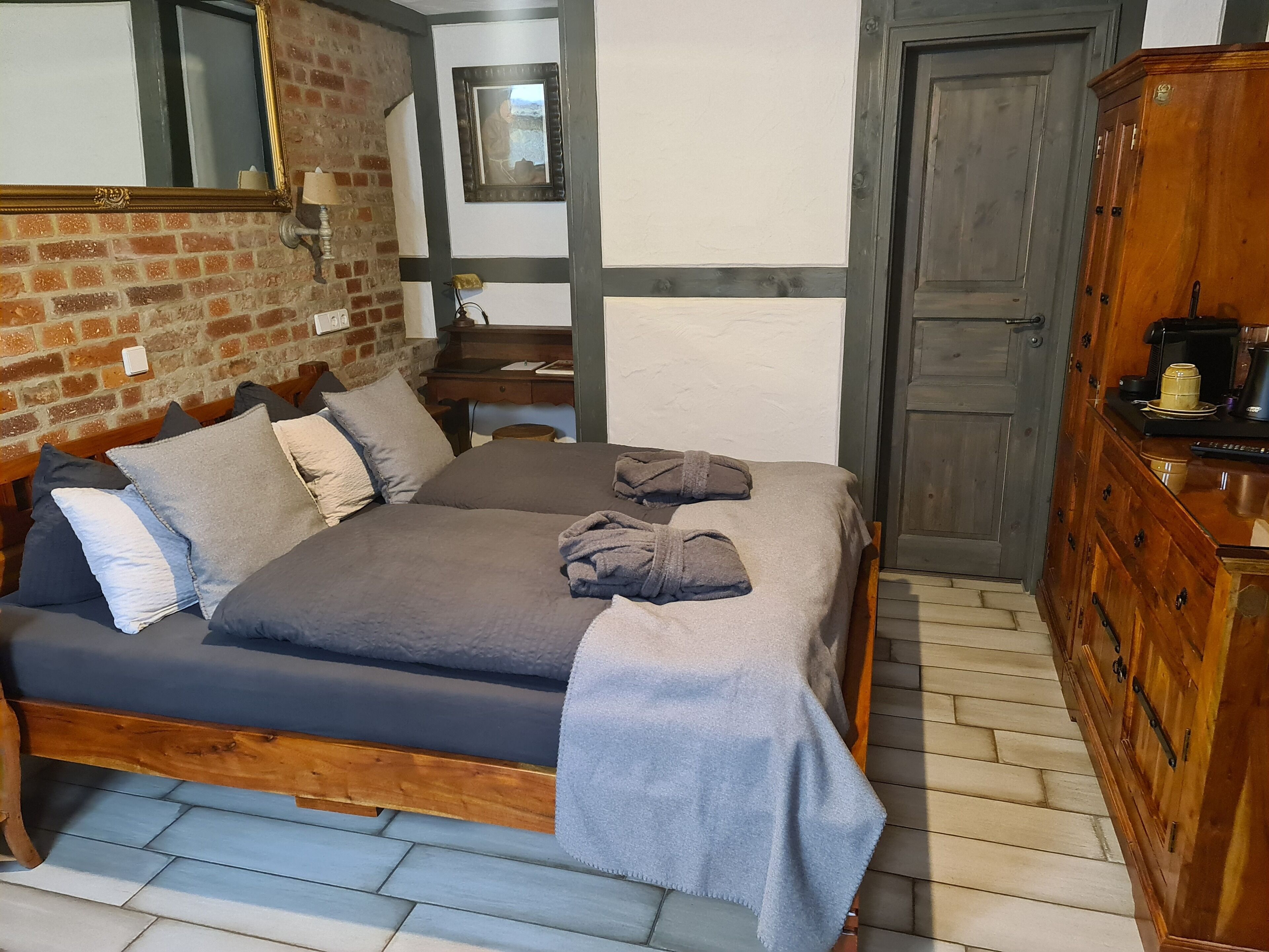 Un dormitorio con una cama de madera, pared de ladrillo, espejo y armario de madera.