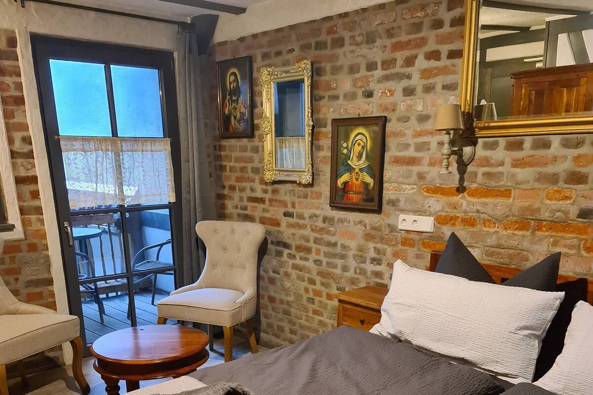 A bedroom with a large bed, a chair, a small table, and a balcony with chairs.