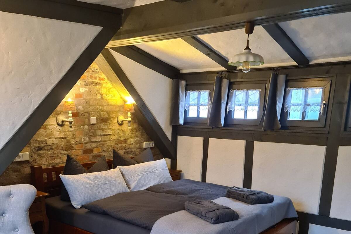 A cozy attic bedroom with a wooden bed, a chair, and a small table.
