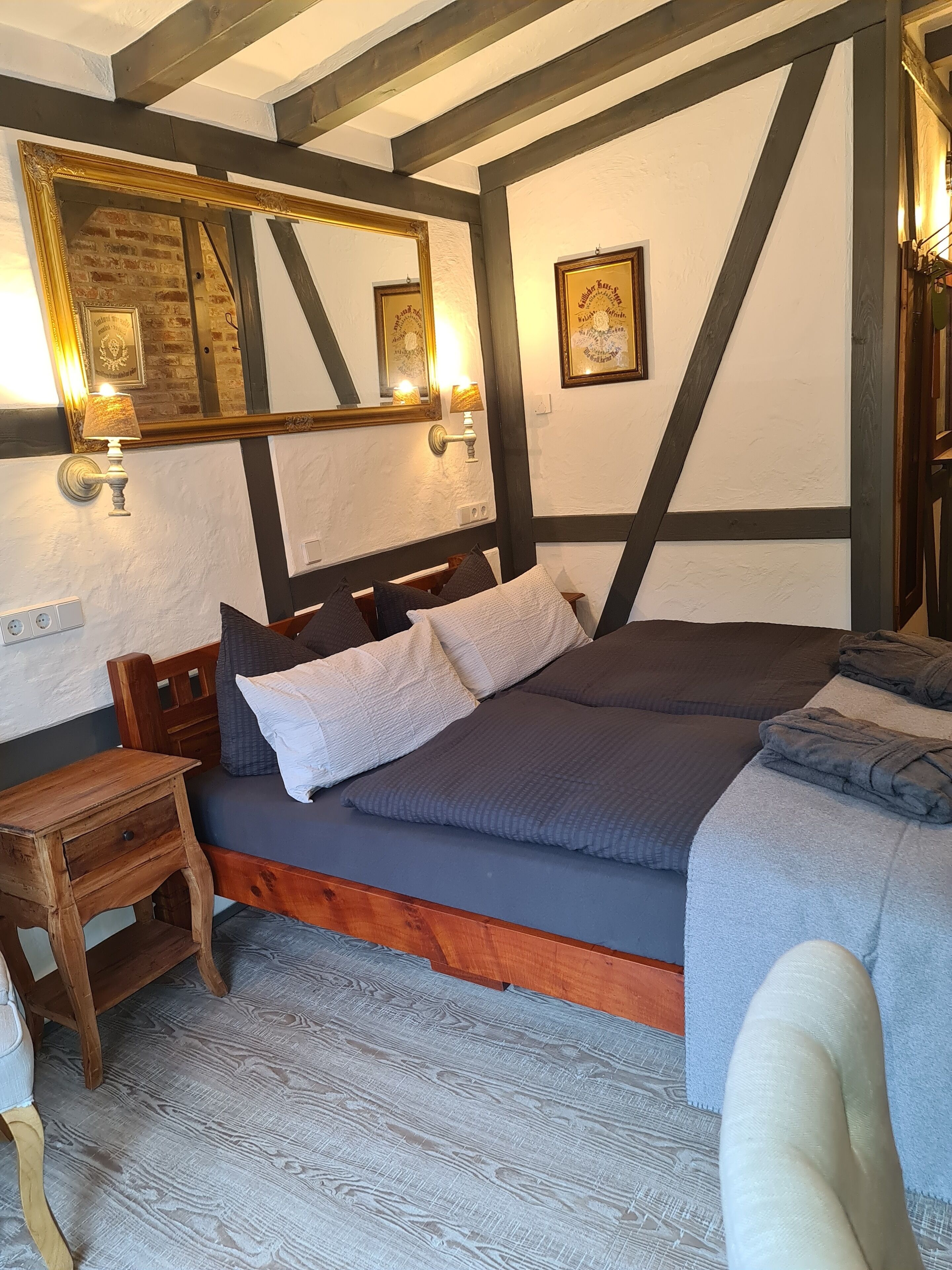 Une chambre avec un grand lit, une tête de lit en bois et un miroir agrémenté d’appliques murales.