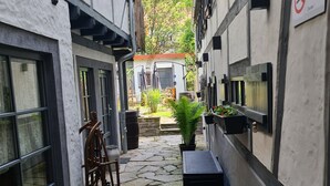 A narrow stone-paved courtyard with a wooden rocking chair, a potted plant, and a metal barrel. - Hotel b&b altes hinterhäusel  (Freiberg)