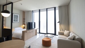 A modern hotel room with a bed, a TV, a sofa, a dining table, and large windows with curtains. - Snug Studio at Upside Living Business Travel Ready (Dubai)