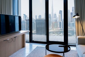A modern hotel room with a large window offering a city view, a flat-screen TV, a small round table, and a sofa. - Snug Studio at Upside Living Business Travel Ready (Dubai)