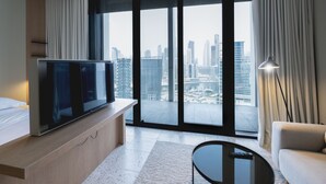 A modern hotel room with a large TV, a sofa, a coffee table, and a city view through floor-to-ceiling windows. - Snug Studio at Upside Living Business Travel Ready (Dubai)