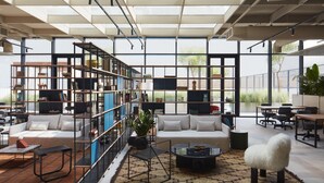 A modern living room with a large bookshelf, a sofa, a coffee table, and a white furry chair. - Snug Studio at Upside Living Business Travel Ready (Dubai)