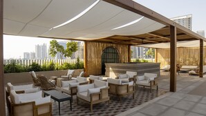 A rooftop lounge with wicker furniture, a bar, and a view of the city skyline. - Snug Studio at Upside Living Business Travel Ready (Dubai)