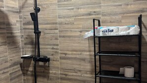 Un baño con ducha, inodoro y estantes con artículos de aseo.