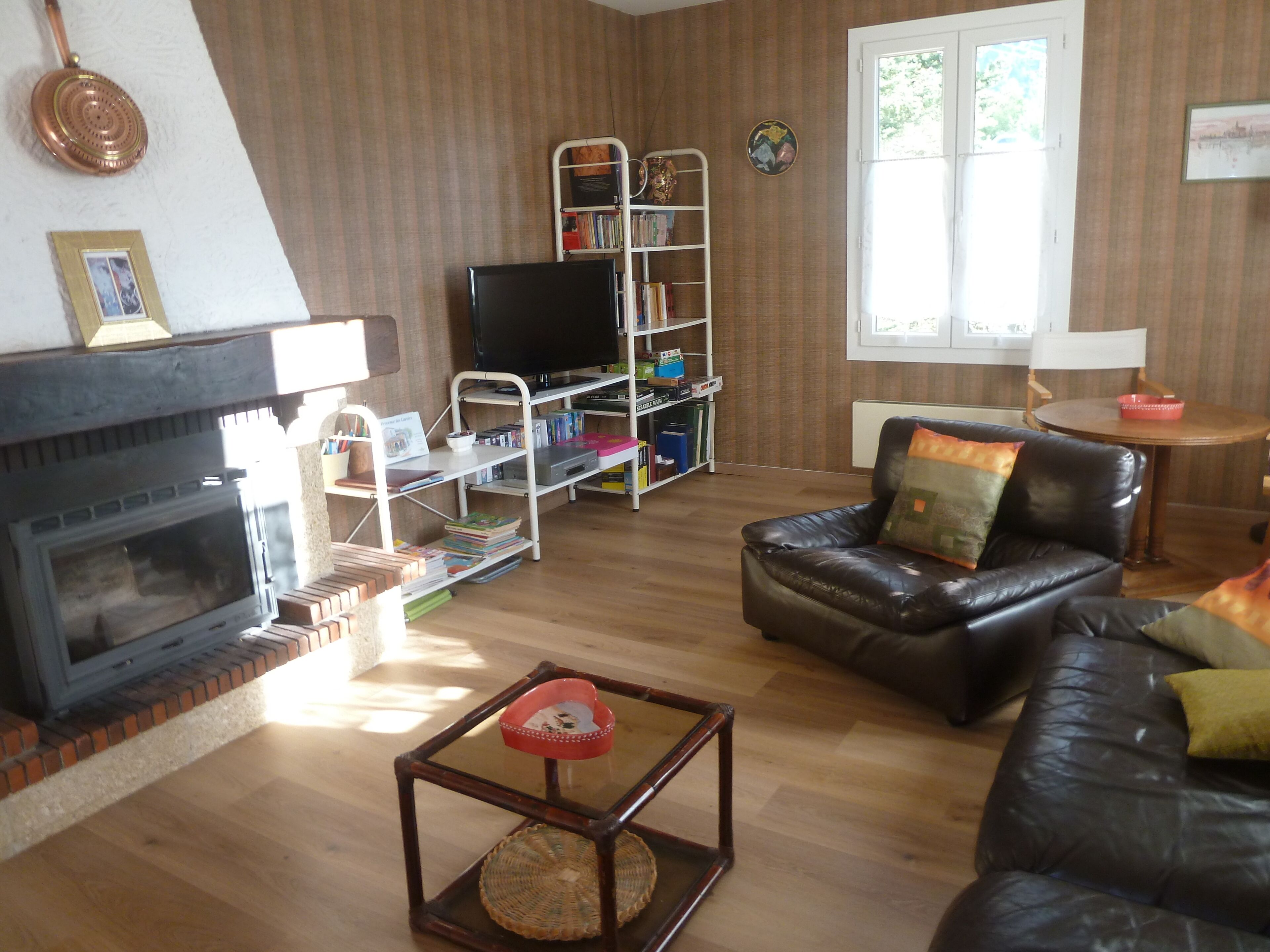 Een woonkamer met een open haard, een leren bank, een salontafel, een televisie en een boekenkast.