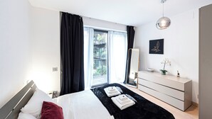 Ein modernes Schlafzimmer mit Bett, Kommode, Spiegel und einem Fenster mit Vorhängen.