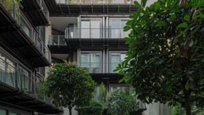 Ein moderner Innenhof mit mehreren Pflanzgefäßen und Bäumen, umgeben von mehrstöckigen Gebäuden mit Balkonen und großen Fenstern.