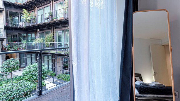 Ein modernes Schlafzimmer mit großem Fenster, einem Spiegel und einem Balkon mit Pflanzen.