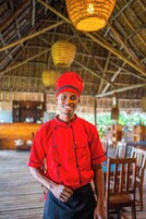 Una persona con uniforme de chef rojo parada en un restaurante con techo de paja y mobiliario de madera.