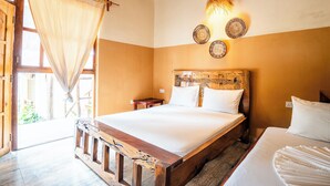 A bedroom with a wooden bed frame, a wooden headboard with decorative carvings, a bedside table, and a wall-mounted light fixture. - La Fotana Restaurant And Bungalows (Kendwa)