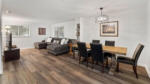 Ein modernes Wohnzimmer mit einem Ecksofa, einem Esstisch mit Stühlen und einer Deckenleuchte.